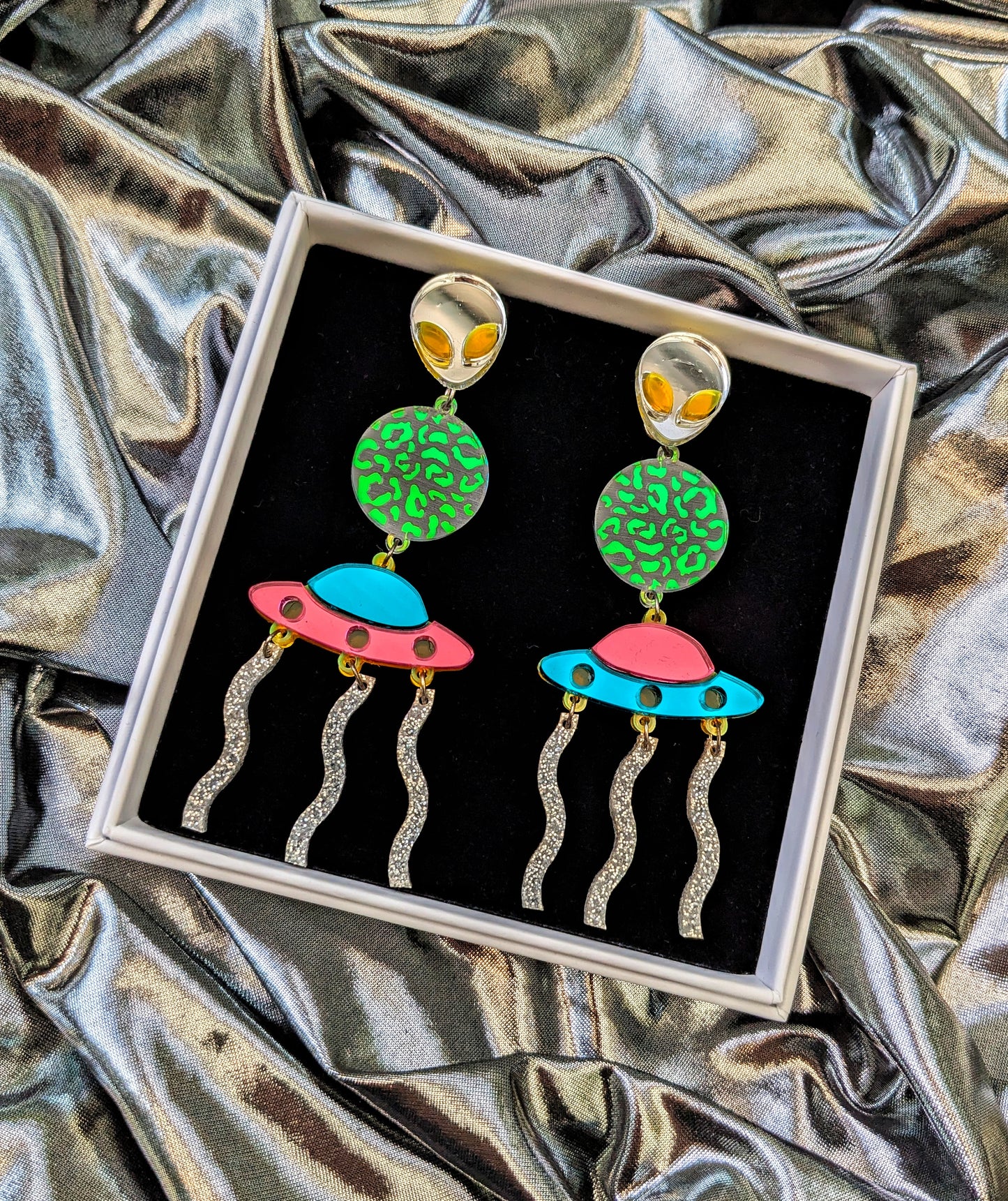 Silver Lasers Statement Earrings with silver and neon green acrylic Alien, a transparent planet with iridescent mermaid acrylic leopard print detailing, Mismatching Pink and Turquoise Mirrored Acrylic Spaceship, and silver sparkly acrylic laser beams